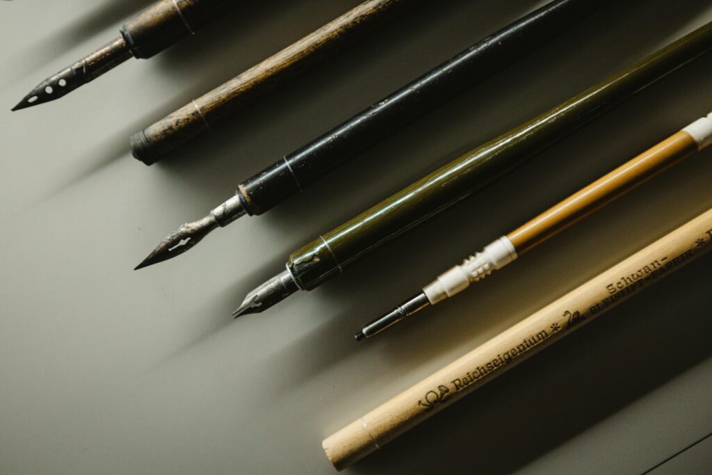 首頁 Close-up of vintage fountain pens and calligraphy nibs on a desk, showcasing writing tools.